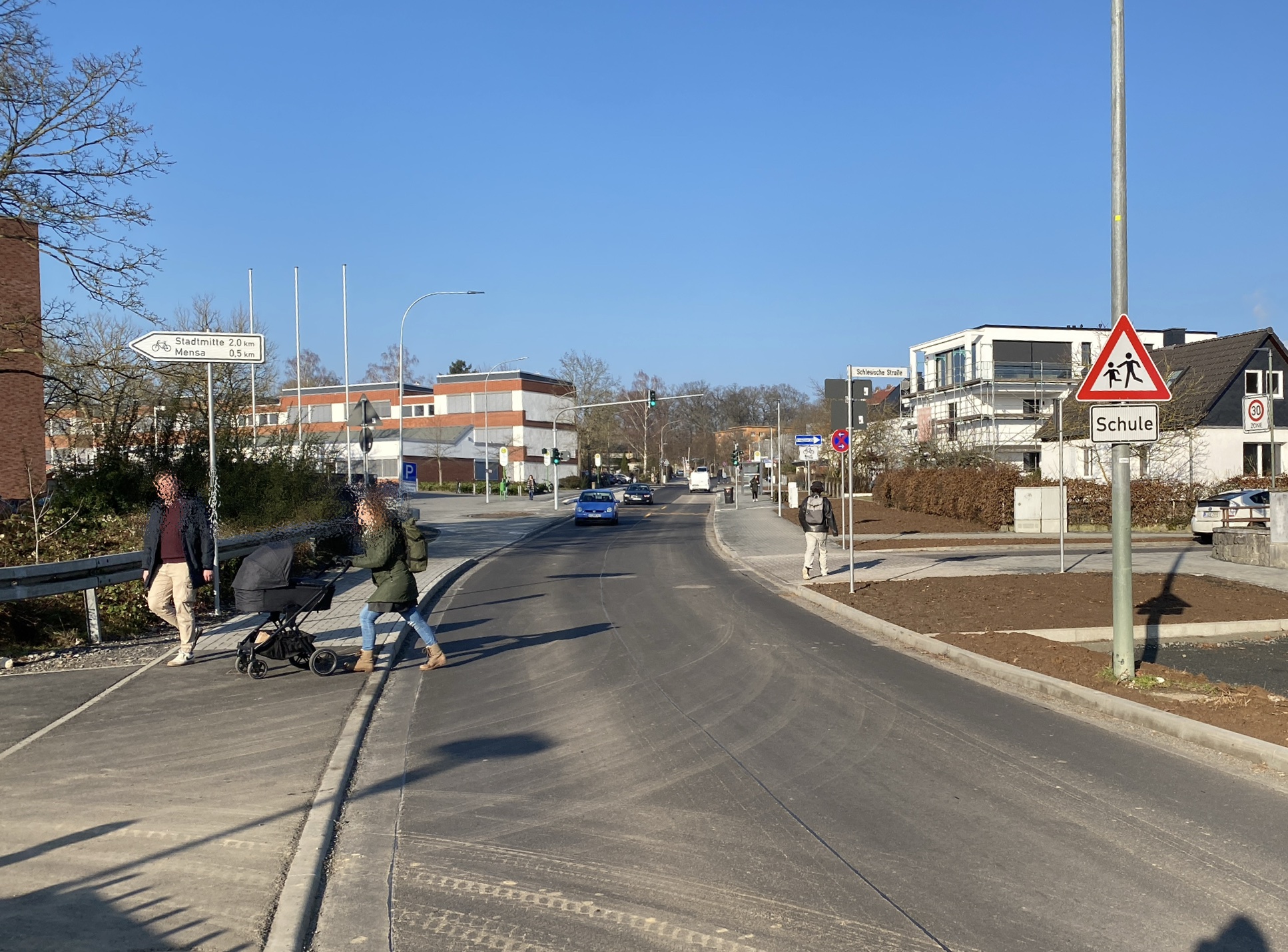 Drei Personen, queren zu Fuß den Alten Steinberger Weg in Höhe Schlesische Straße. 